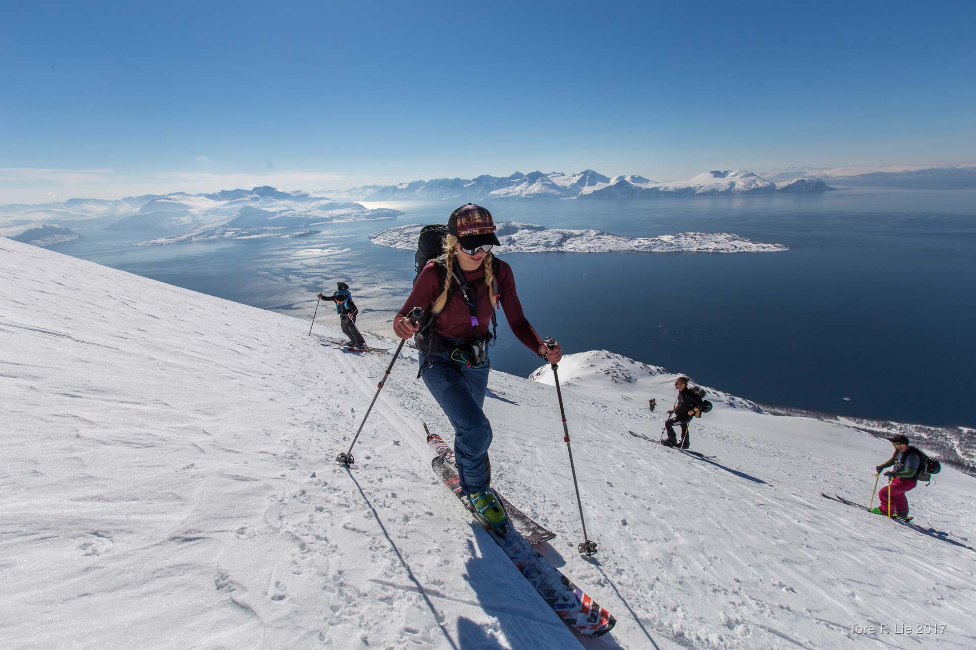 Christine skinning up a snowy ridge above a fjord