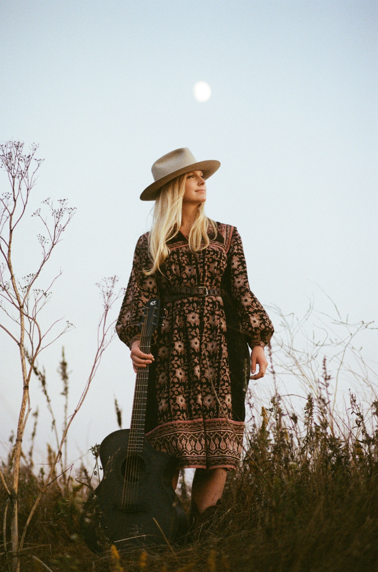 Christine standing in a field with guitar under a moon